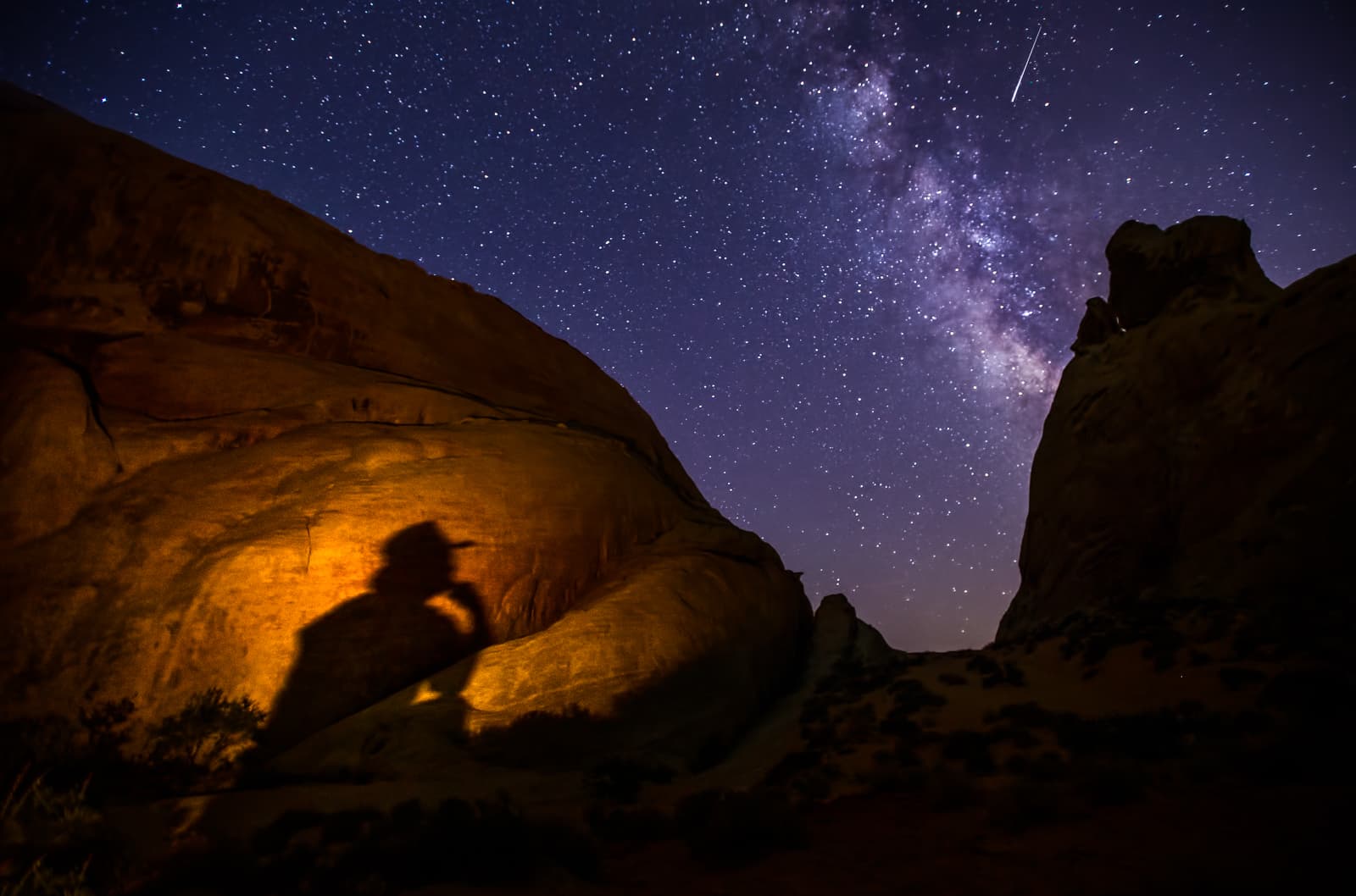 The Milky Way above desert rock, with the photographer's shadow light-painted on the stone