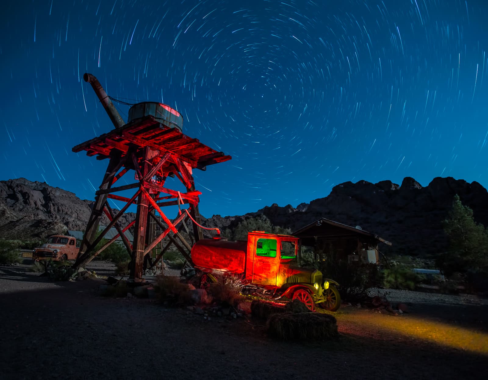 Star trails circling above a light-painted mining rig and vintage tanker truck
