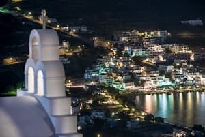 A white Greek church at night above the lights of Aigiali, Amorgos